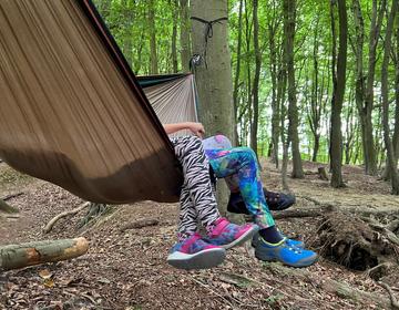 The legs of two children dangle over the edge of a hammock strung between trees.