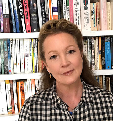 Charlie Lee Potter stands in front of a bookcase, wearing a checked shirt