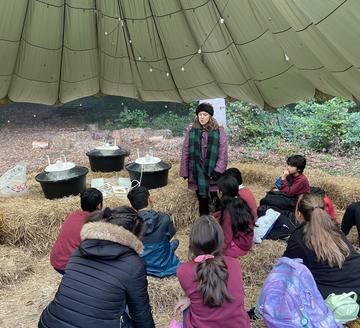 A group of school pupils listen to an expert while sitting on haybales. Three moth traps are positioned nearby