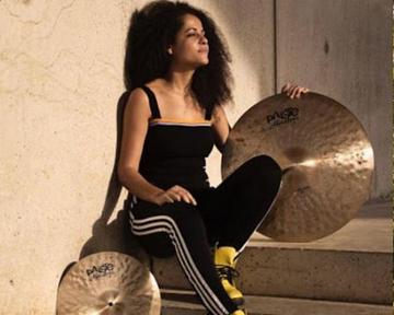 Jas sits on a step, holding a cymbal