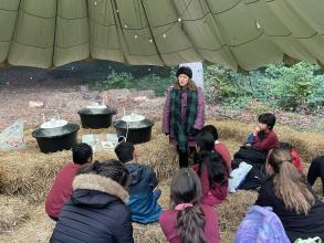 A group of school pupils listen to an expert while sitting on haybales. Three moth traps are positioned nearby